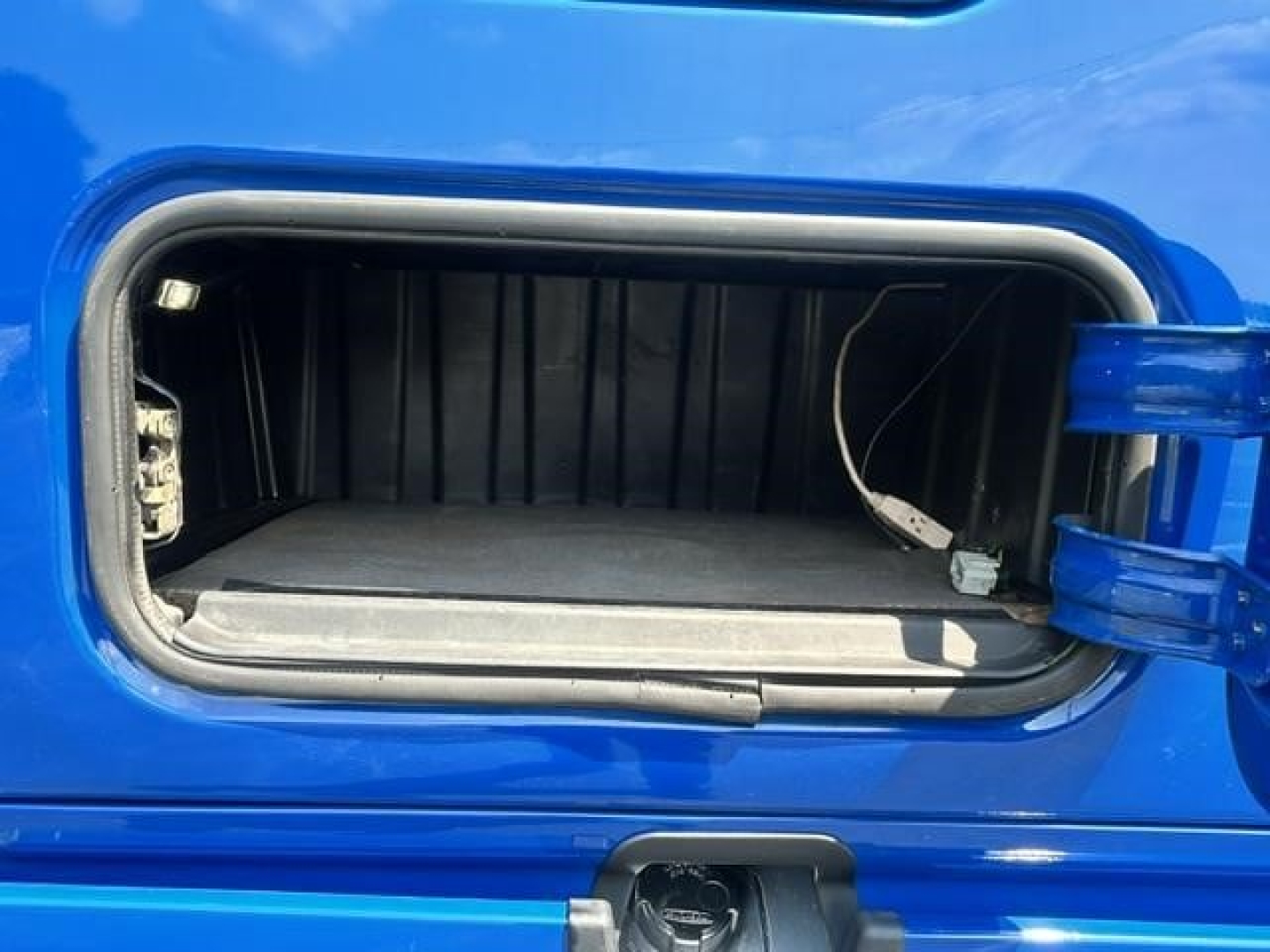 Freightliner Cascadia 126 sleeper truck front storage/storage bay open with blue exterior. The image shows an empty front storage compartment or bay with a small cable inside.