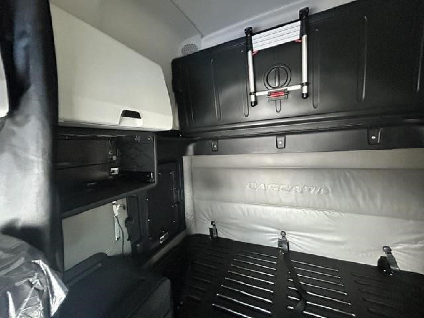Freightliner Cascadia cab interior with sleeper area showing storage shelves and overhead cabinet. Text visible: 'MATRIX' or 'MATRA' on bed wall; no other legible labels.