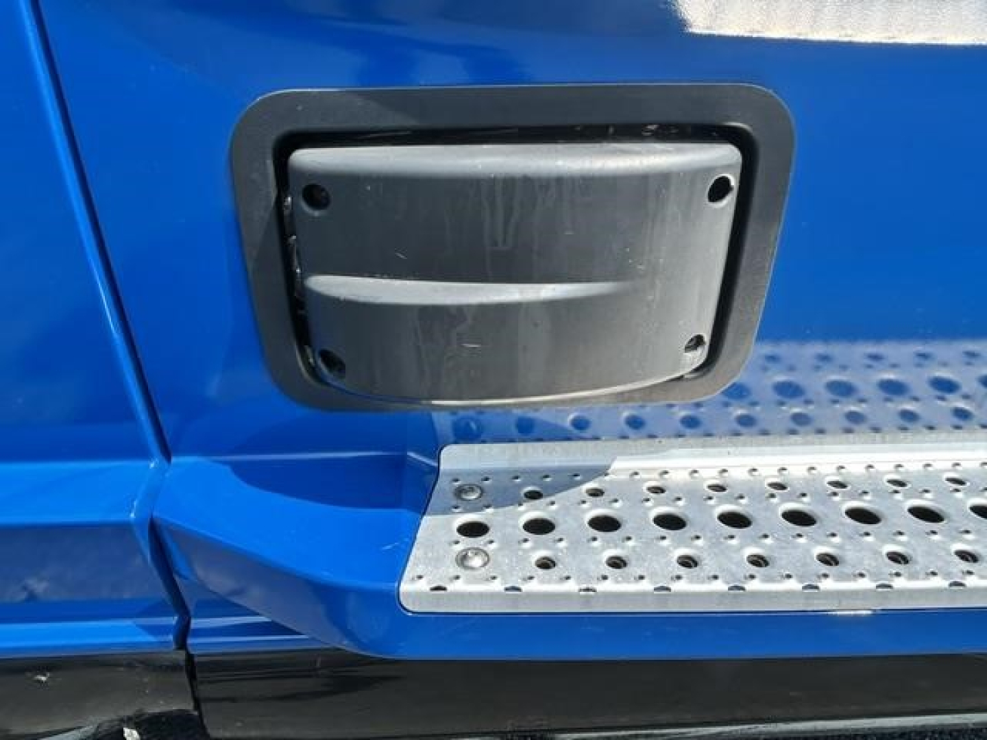 Truck exterior door area showing a black rectangular access panel on a blue Freightliner Cascadia cab with metal running board perforations.