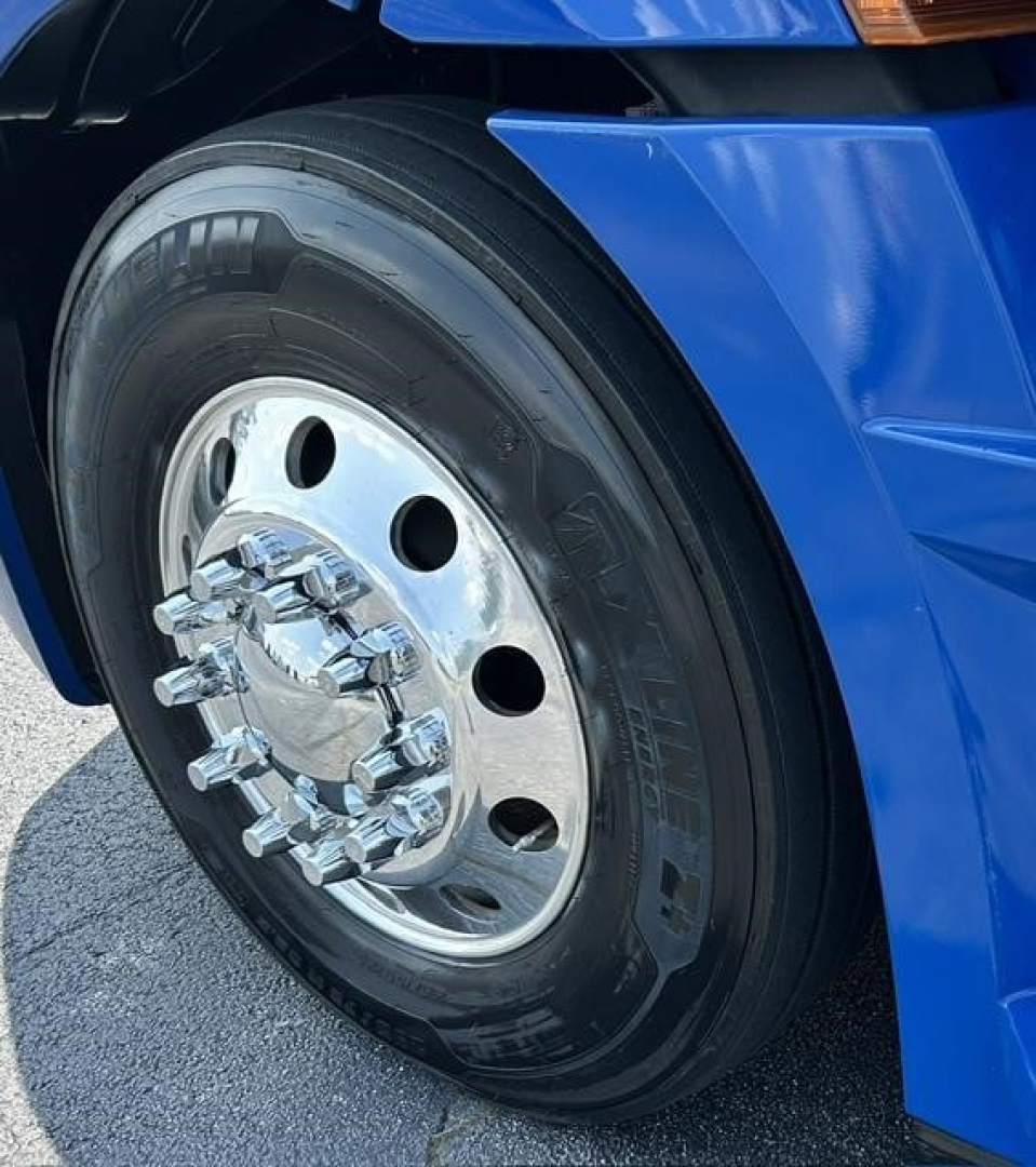Freightliner Cascadia 126 front wheel showing chrome hub, black tire, blue fender and wheel cover
