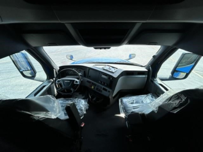 Cab interior of a 2022 Freightliner Cascadia 126 sleeper showing steering wheel, dashboard, and plastic-covered seats.