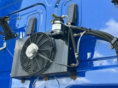 Freightliner Cascadia 126 engine bay area showing radiator (cooling fan) and air conditioning compressor mounted on blue truck side with hoses and wiring.