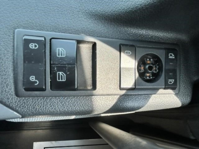 Truck interior panel showing window/lock controls and circular knob. Visible text on switches includes window icons, lock icons, and a 12V/auxiliary style socket area.