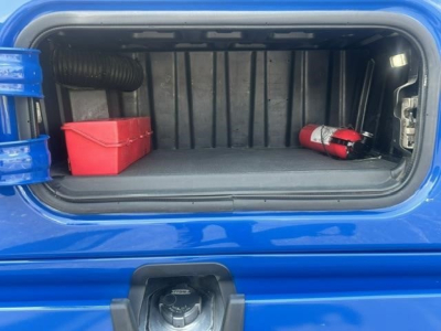 Truck cab storage area showing open side fuel tank cavity with red storage bin and a fire extinguisher mounted inside.