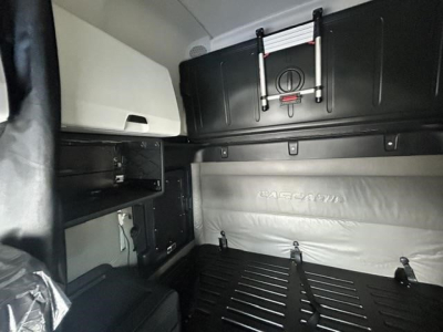 Freightliner Cascadia cab interior with sleeper area showing storage shelves and overhead cabinet. Text visible: 'MATRIX' or 'MATRA' on bed wall; no other legible labels.
