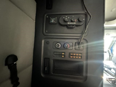 Cab interior panel of Freightliner Cascadia with control knobs and small display, showing vents and switches.