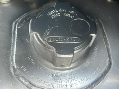 Fuel cap on Freightliner Cascadia engine bay showing DEF/fuel filler cap with warnings and text around it.