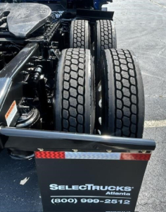 Truck rear chassis with dual rear axles and dual tires visible beneath; SelectTrucks Atalanta logo plate and contact number at rear fender.