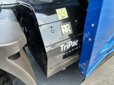 Truck equipment image showing TriPac Evolution auxiliary power unit under Freightliner Cascadia hood area with sticker and Toyota-like logo; black enclosure with yellow label.
