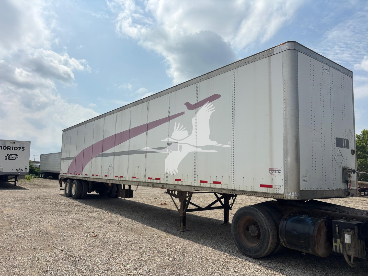 Trailer side view showing large white and pink graphic, two-axle gooseneck? No, semi-trailer with van body and landing gear visible.
