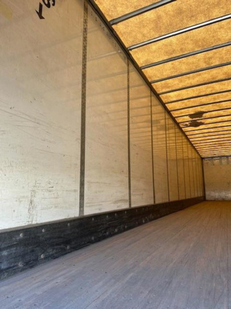 Trailer interior showing empty cargo van with wooden floor and side panels, warehouse lighting reflections, and ceiling ribs.