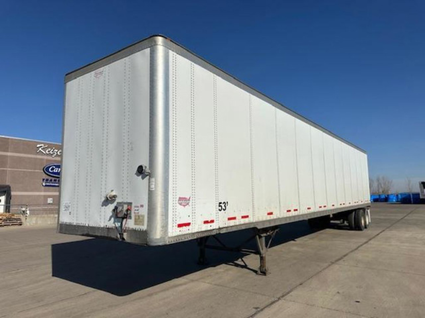 Semi trailer in a parking lot showing a white Wabash box with 53' length marking, rear and side reflective tape, and hitch/kingpin area.