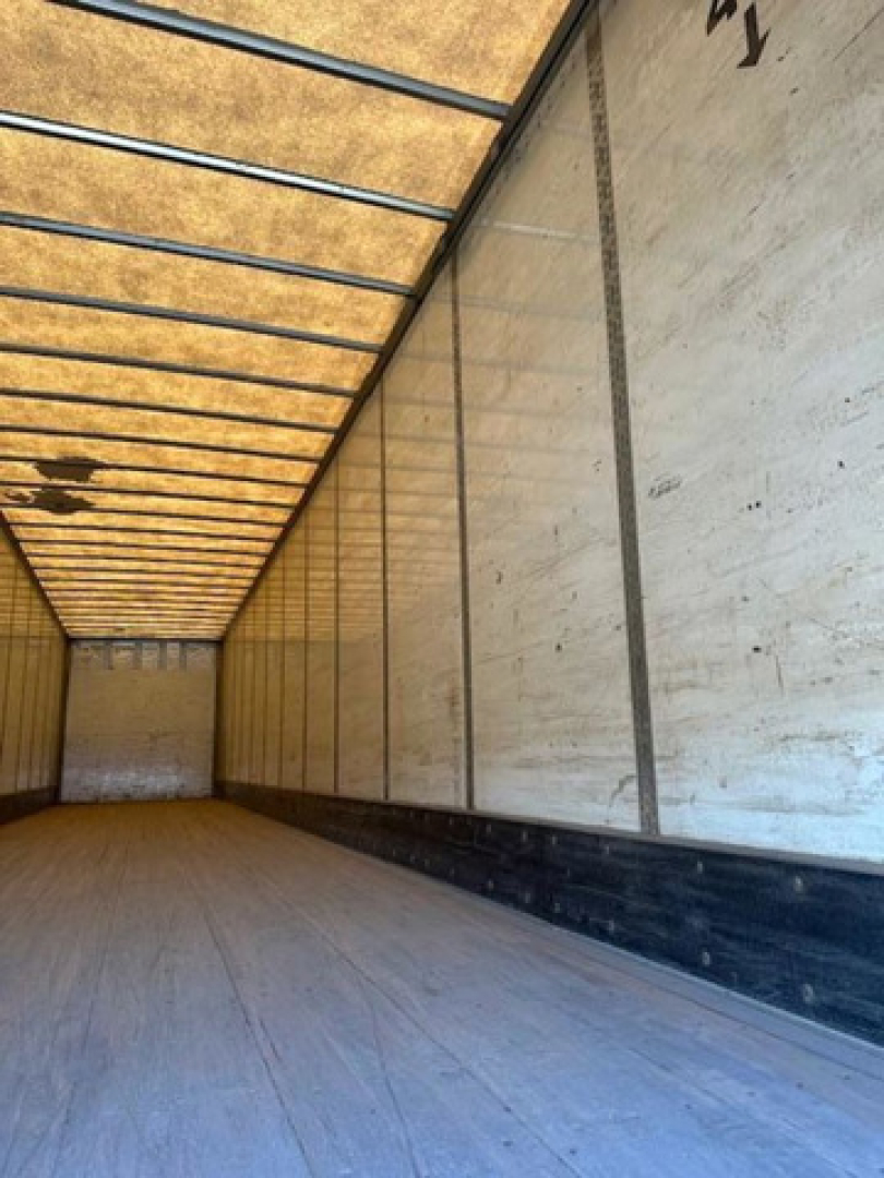 Empty interior of a Wabash trailer with white walls, wooden ceiling framing, and a light gray floor.