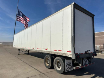 Trailer rear-left view showing a white Wabash van trailer with dual rear axles, US flag, and registration numbers on bumper.