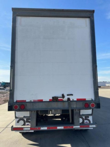 Trailer rear view showing white cargo area with bumper lights and rear underride guard, concrete ground, blue sky.