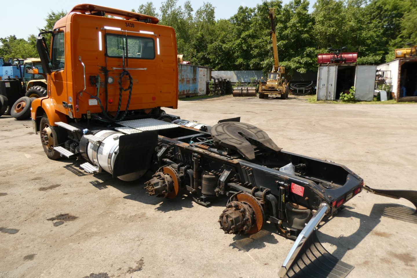 Orange Volvo VNM64T truck cab with exposed chassis and rear suspension, no trailer, in yard.