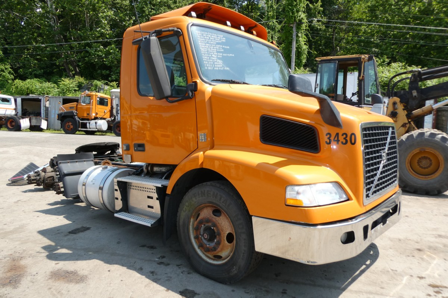 Volvo VNM64T conventional daycab truck with 3430 number on door and orange cab, front view showing fuel tanks and wheel(s).