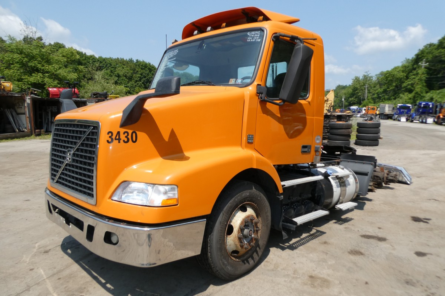 Orange Volvo VNM64T daycab truck with number 3430 on the hood, showing cab and fuel tanks, front grille, headlights, and side view.
