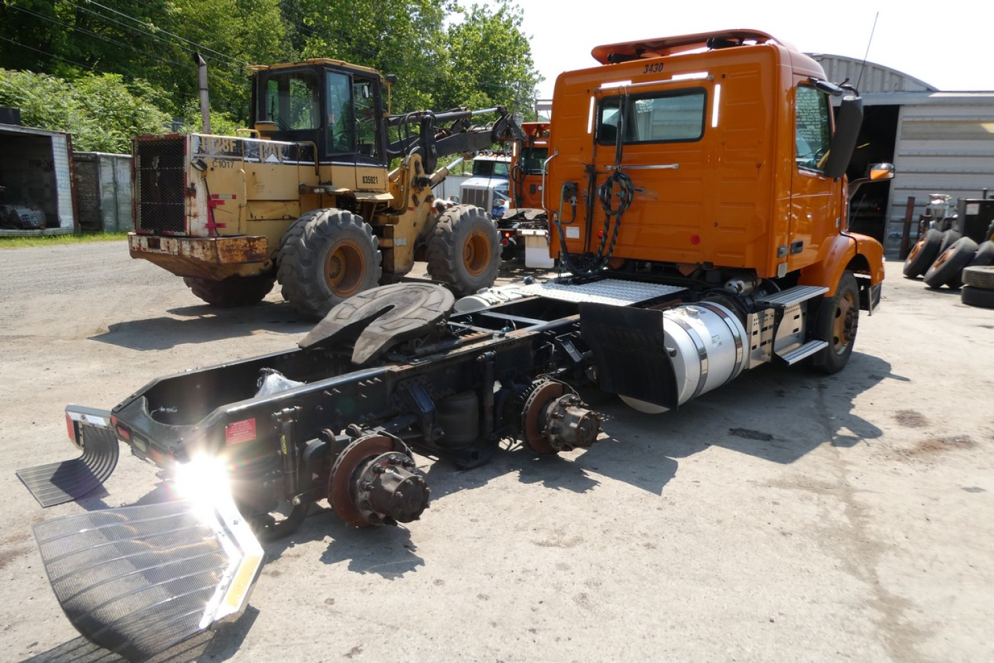 Volvo VNM64T truck cab and chassis in a yard showing exposed front axle and drivetrain components.