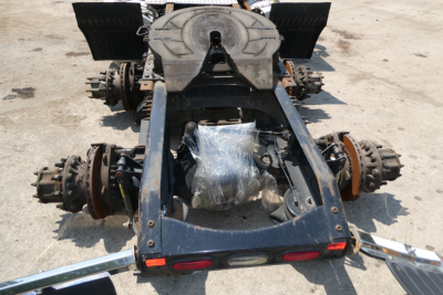 Truck chassis rear view showing frame, axles, and suspension components with wrapped driveline on a concrete surface.