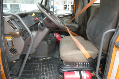 Volvo VNM64T truck cab interior showing driver seat and steering wheel with orange seatbelt across seat and dashboard controls visible.