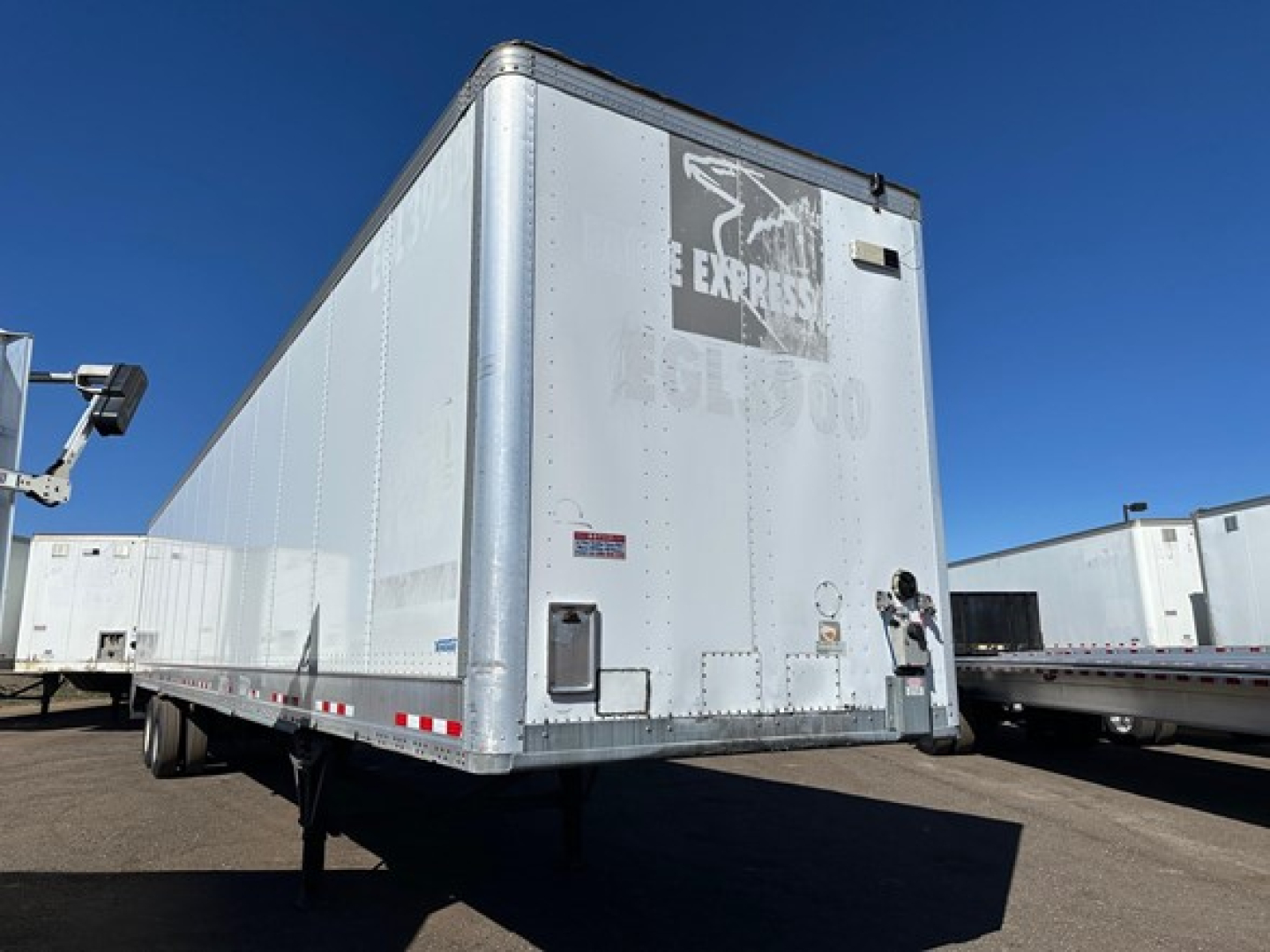 Trailer rear view showing Vanguard dry van with roll-up door, aluminum exterior, side marker lights, and tandem axles under a clear sky.