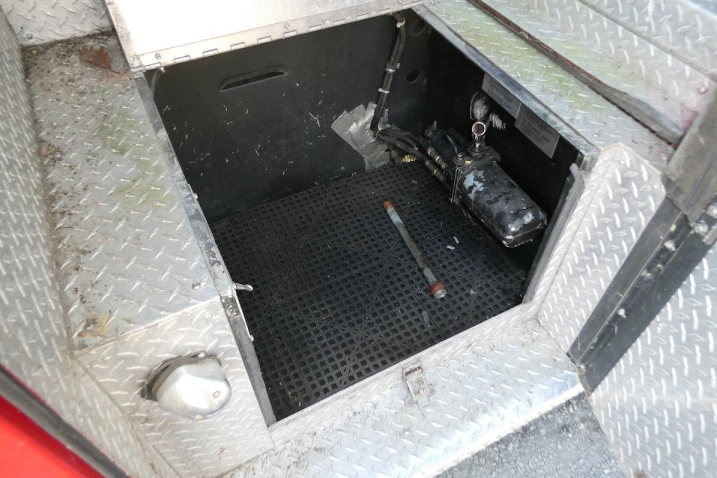 Fire truck crew area with diamond plate flooring and control lever; tools and hydraulic components visible in side compartment.