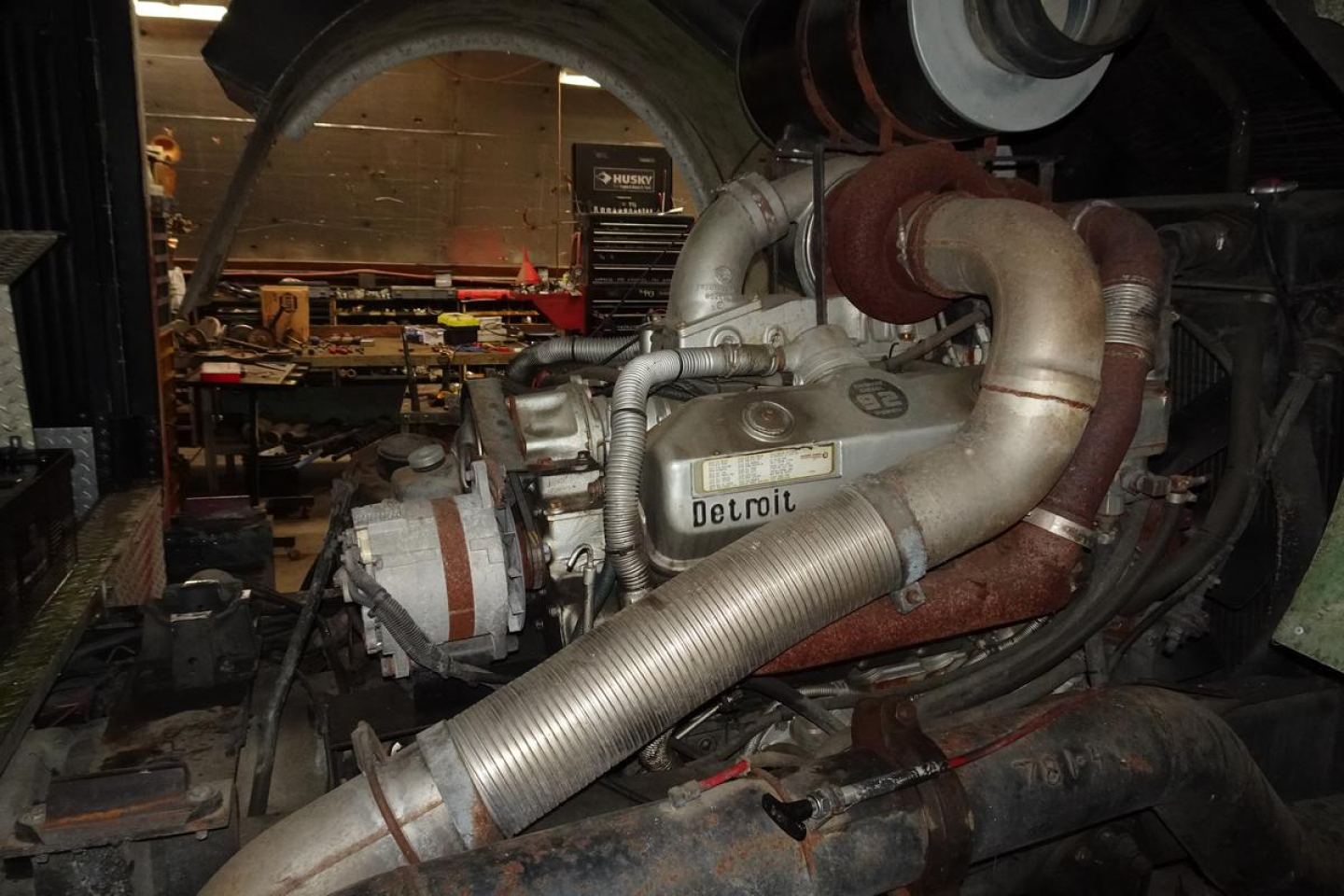 Engine bay of a 1991 KME fire truck showing large intake hose and Delco-style engine with metal tubing and exhaust piping.