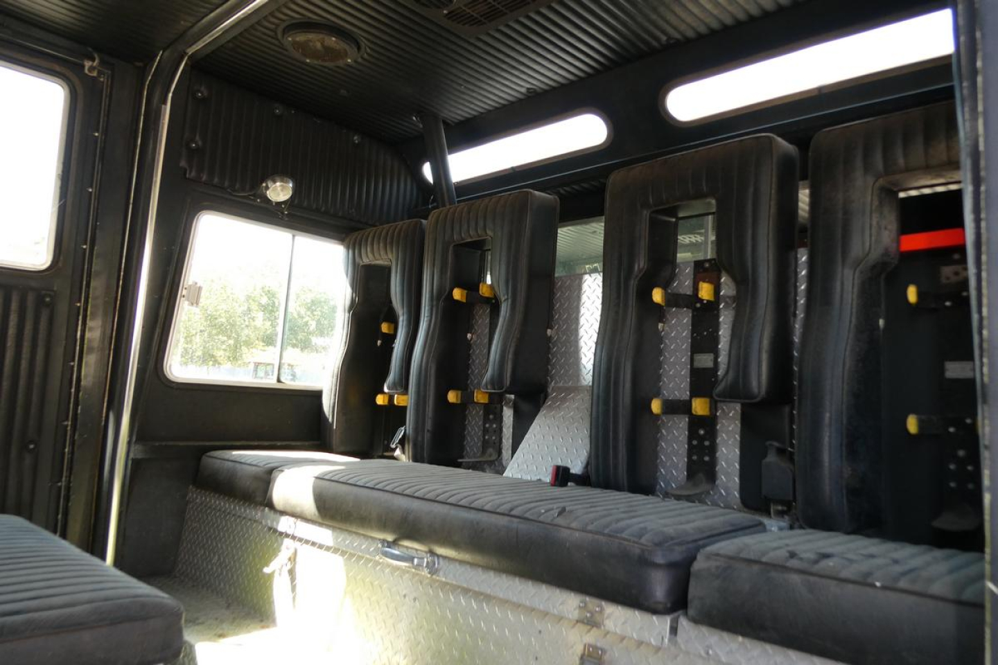 Fire truck interior showing seating for multiple firefighters with black padded seats and yellow restraints.