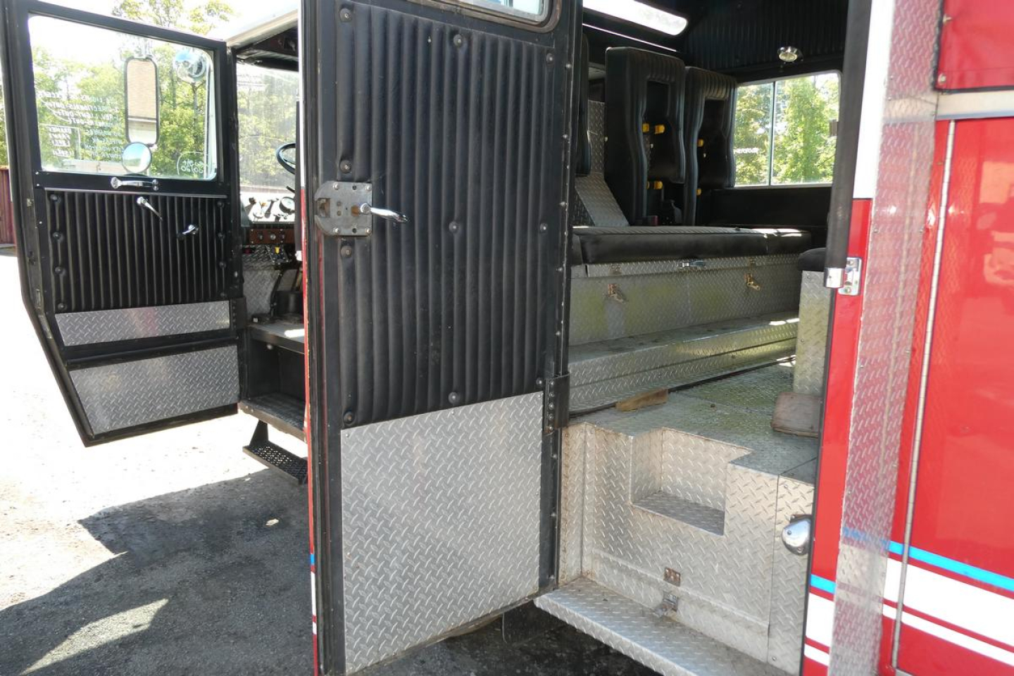 Fire truck interior showing rear cab seating and open doors with metal diamond-plate panels and storage compartments.