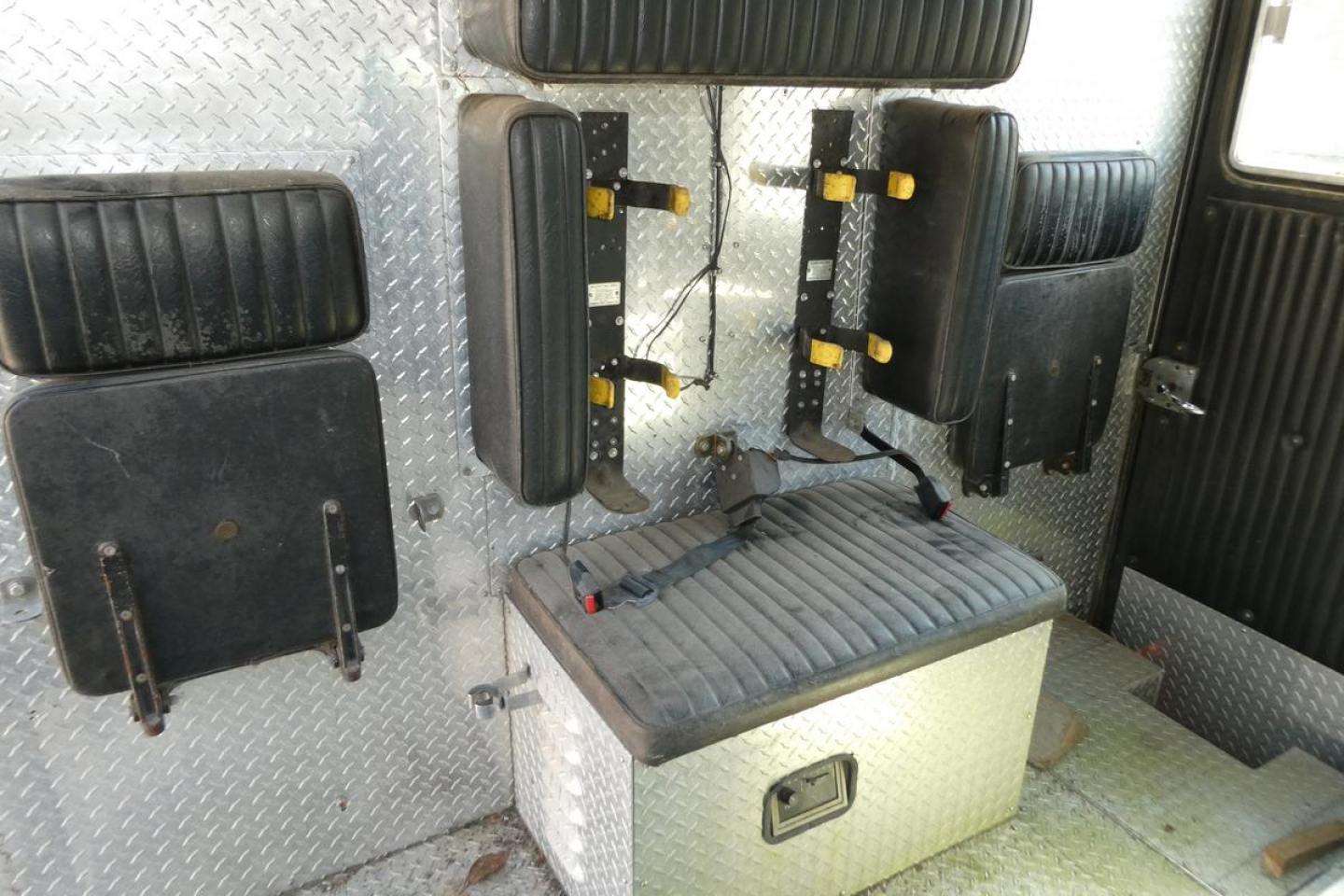 Truck interior showing seating and diamond plate walls with mounted black seats and a silver toolbox.