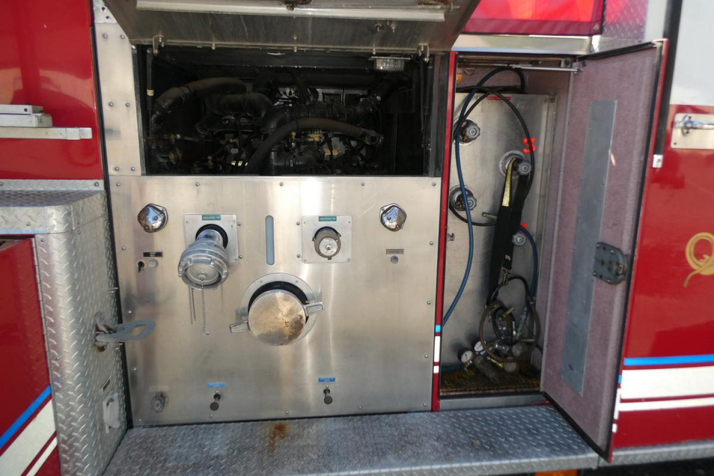 Truck rear body panel with pump controls and access door showing gauges and hoses on a fire truck, including engine bay view and storage area.