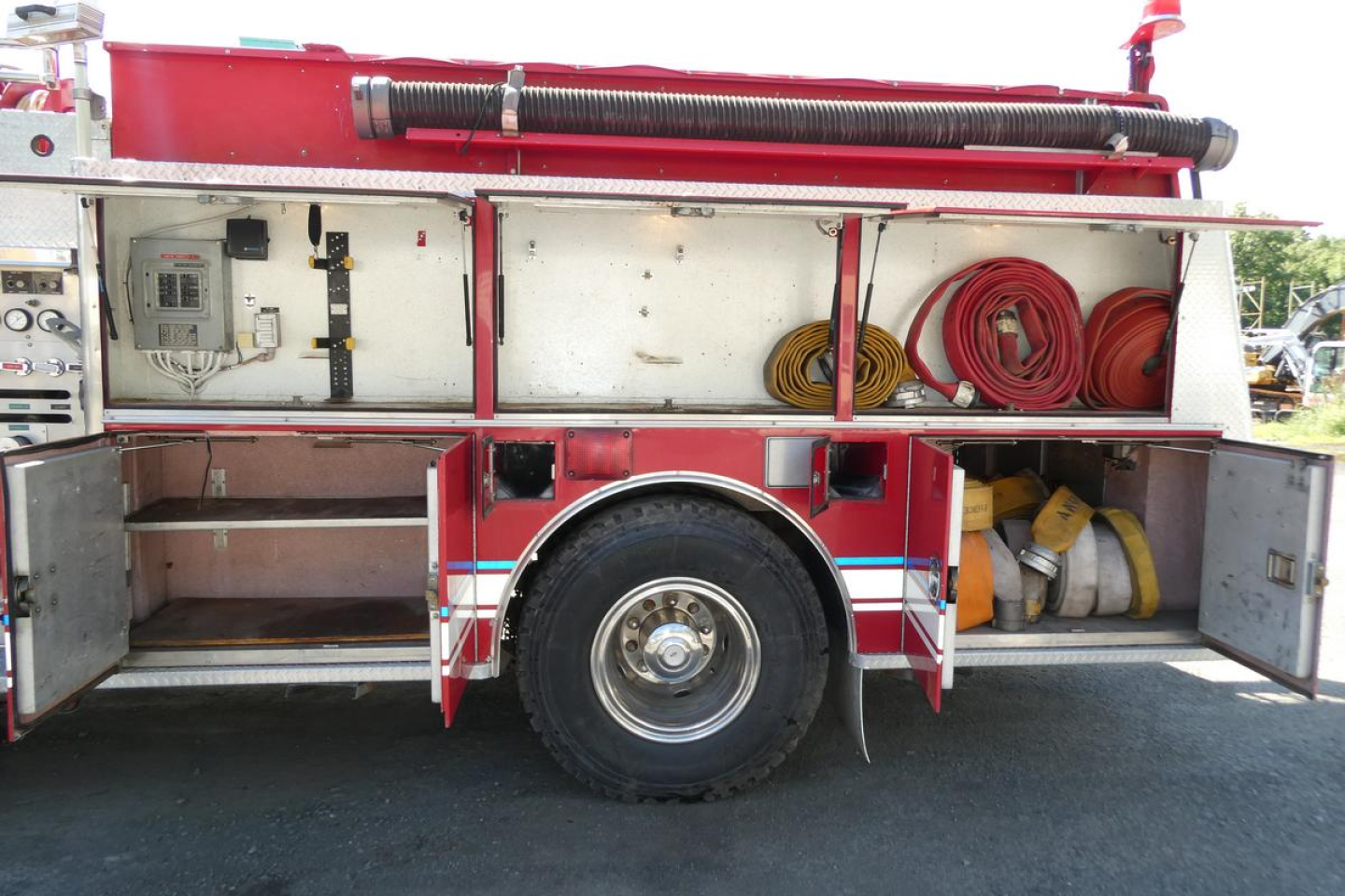 Rear side of a 1991 KME fire truck showing compartments with hoses, tool shelves, and a spare hose reel.
