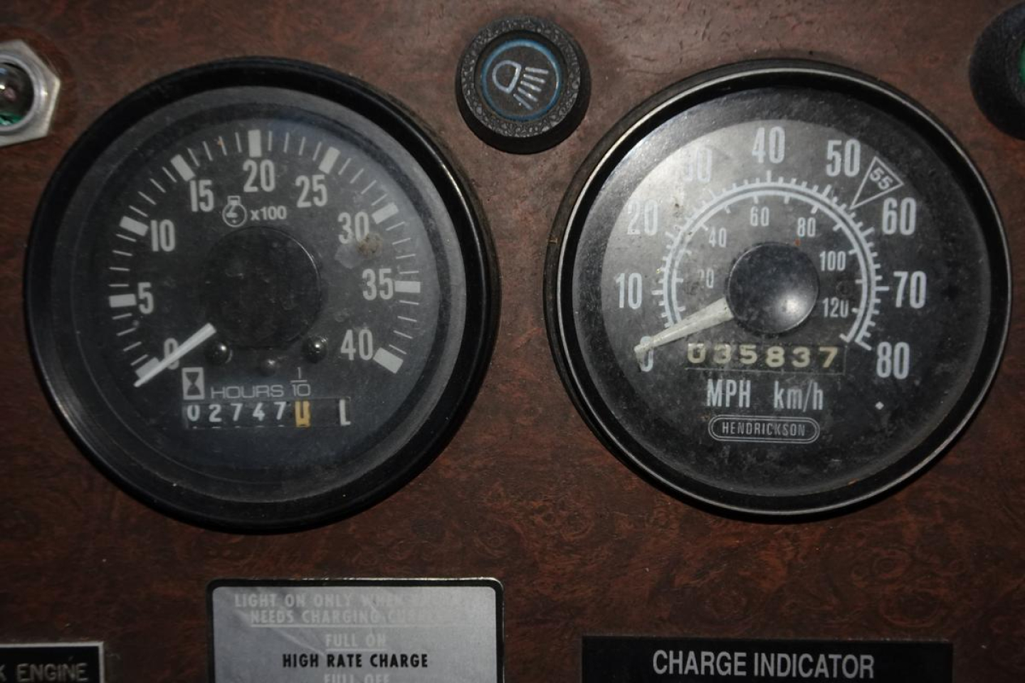 Dash gauges showing hours and speed on a vintage fire truck. Left gauge: hours 0 to 40, odometer reads 02747 L; right gauge: speedometer up to 80 mph, odometer reads 003587.05? rpm? and multiple markings. Small indicator lights and labels v