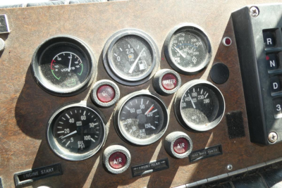 Panel of gauges on a vintage fire truck dashboard showing oil pressure, water, air, and engine temperature gauges with labels such as ENGINE START and THRU-HEAT.