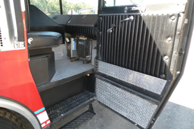 Fire truck interior showing entry steps, diamond plate flooring, and door with vertical rib panels.