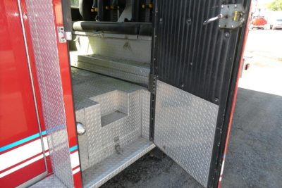 Fire truck rear entry showing diamond plate steps and black rear door with latch, red exterior panels, and interior metal flooring.