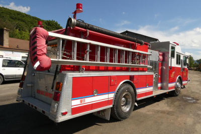 Fire truck in-service rear-right view with hoses and storage compartments visible.