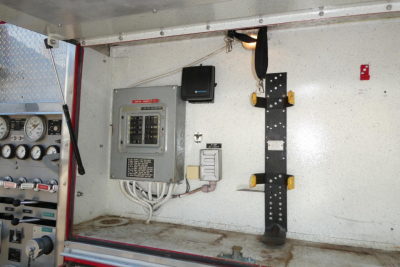 Firetruck service bay interior showing electrical panel, wiring, and rack with yellow pin holders.