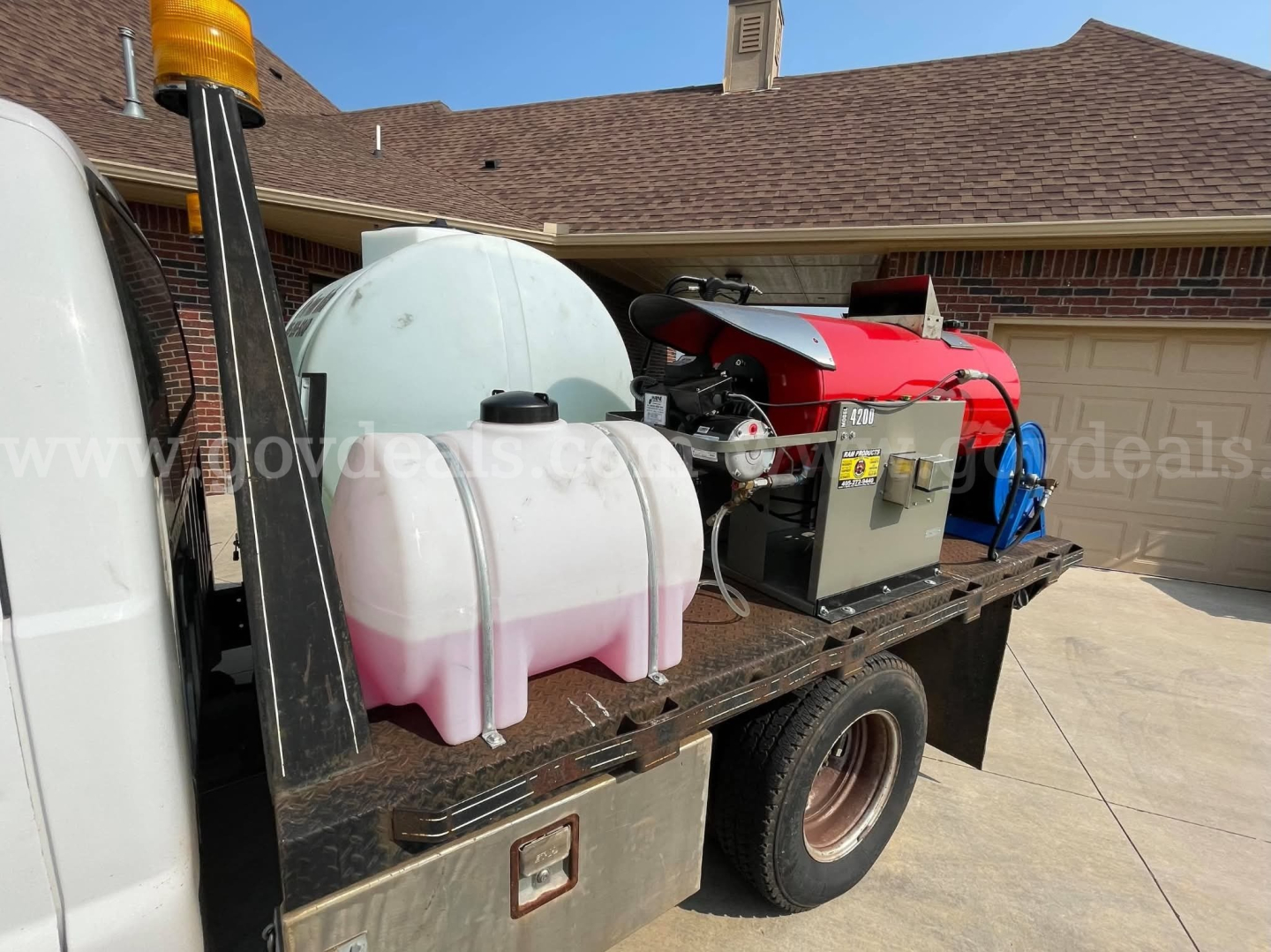Service/utility truck bed with generator, hoses, and white/pink plastic tanks on flatbed; orange warning beacon on left.
