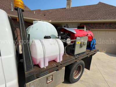 Service/utility truck bed with generator, hoses, and white/pink plastic tanks on flatbed; orange warning beacon on left.