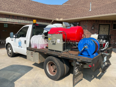 Service/utility truck with a red portable water tank, hose reel, and equipment on the flatbed; Ford logo visible on door; rooftop clearance light; equipment box and hoses.