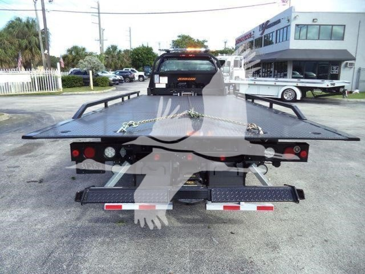 Rear view of a flatbed rollback tow truck with taillights and bumper, stock number visible, in a dealership lot.