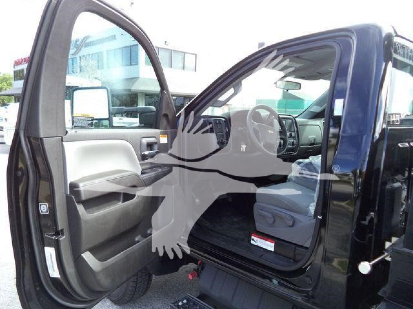 Truck cab interior with open driver door showing dashboard and steering wheel; Chevrolet Silverado 6500HD text not visible.