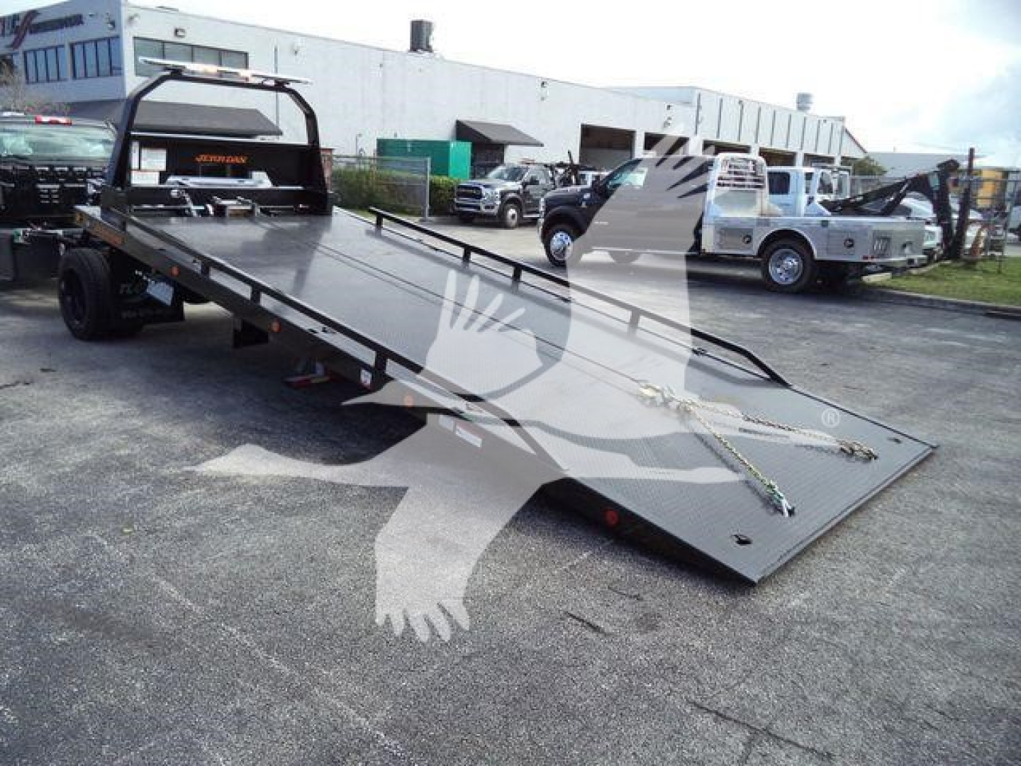 Flatbed tow truck slide bed with ramp extended showing heavy-duty truck in a dealership lot.