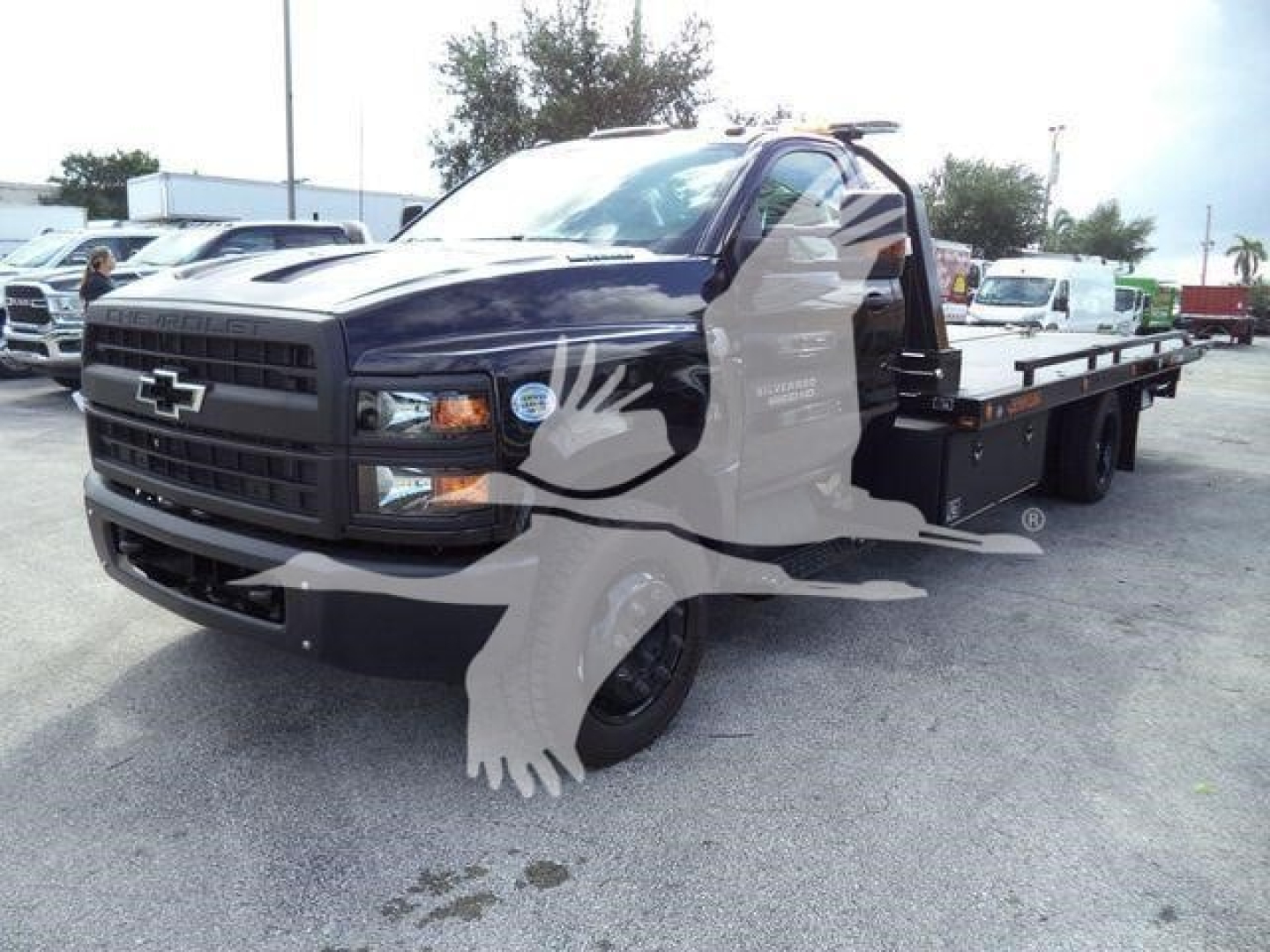 2023 Chevrolet Silverado 6500HD rollback truck with flatbed, front grille with Chevrolet emblem, black exterior, open driver door, stock number visible in listing.