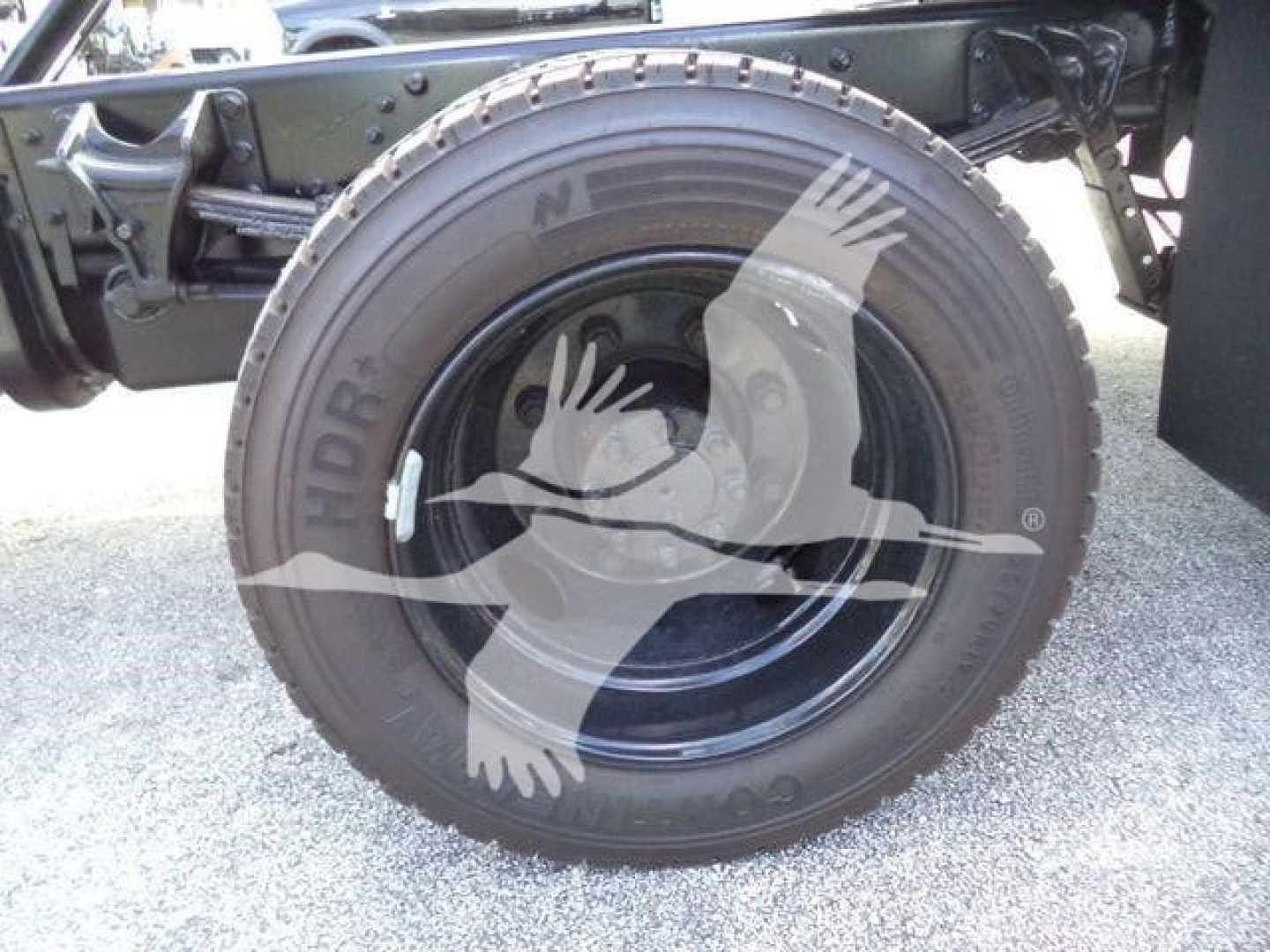 Truck wheel close-up showing spare tire mounted on rollback bed with black steel rim and tire sidewall text.