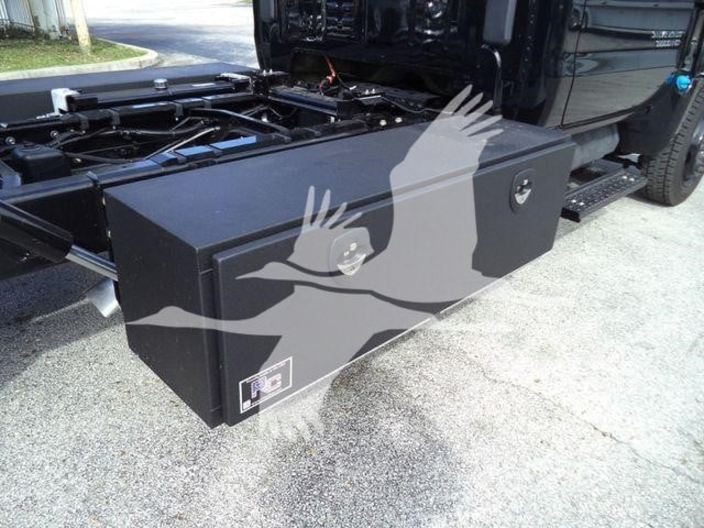 Truck bed toolbox mounted on Chevrolet Silverado 6500HD chassis showing a square black toolbox with a lock and a small label.