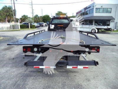 Rear view of a flatbed rollback tow truck with taillights and bumper, stock number visible, in a dealership lot.