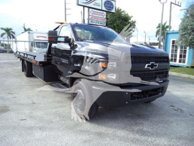 Truck cab and extended flatbed rollback w/ Chevrolet logo on grille; front-right view; black flatbed with wheel lift; daytime dealership lot.